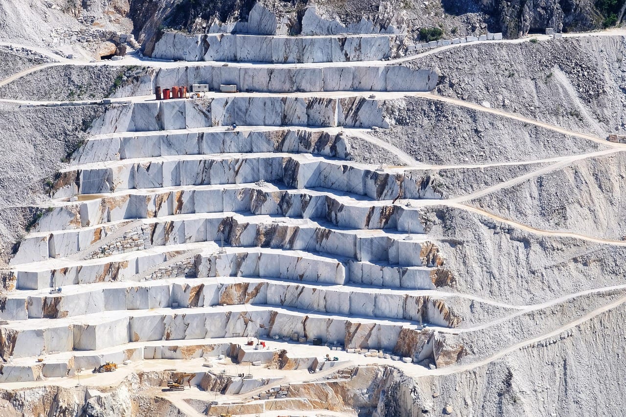 Cantera de mármol en terrazas escalonadas talladas en la ladera de una montaña, con bloques de piedra blanca y caminos de acceso