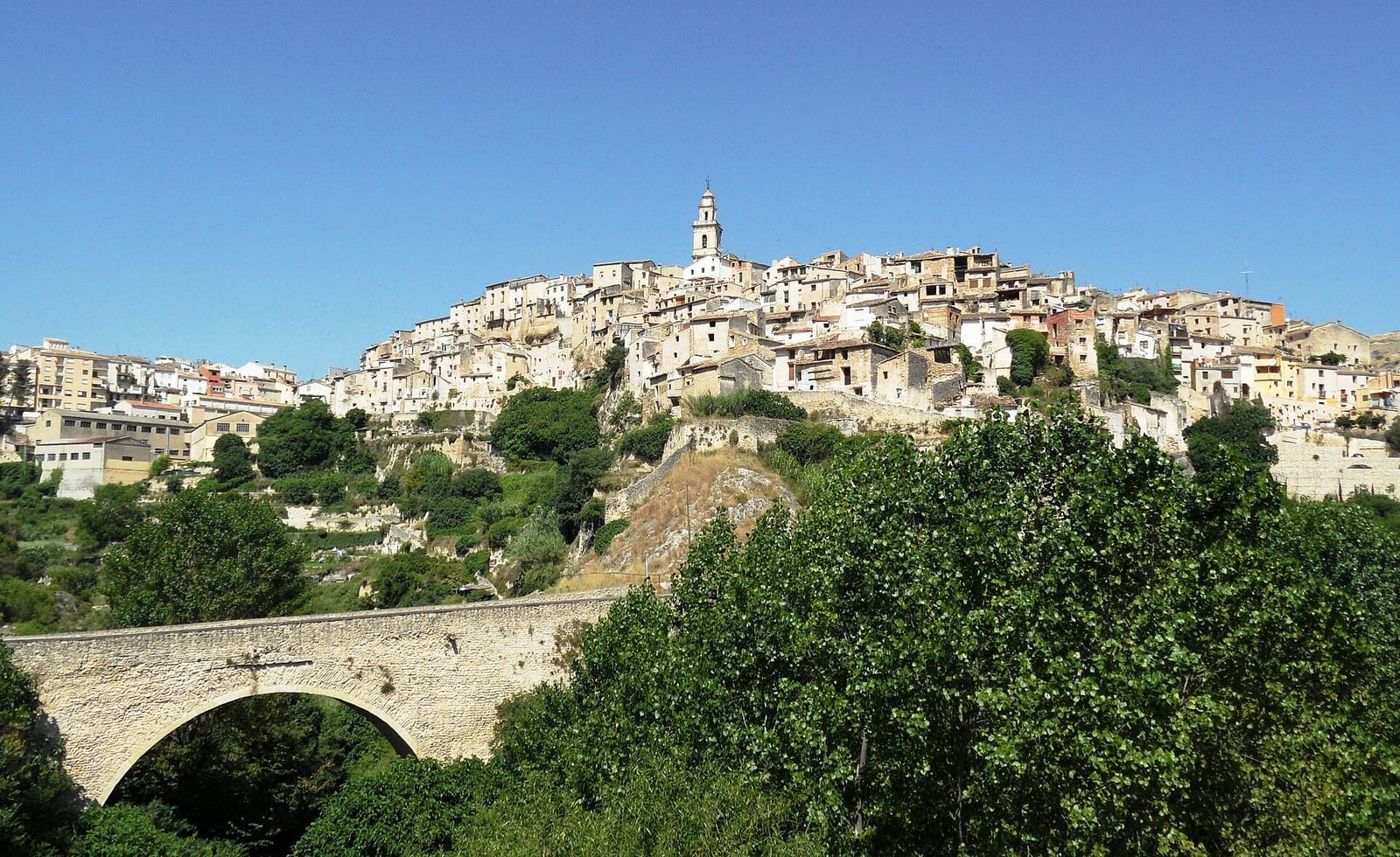 Vista de Bocairent con las casas escalonadas sobre un cerro rocoso y un puente de piedra en primer plano