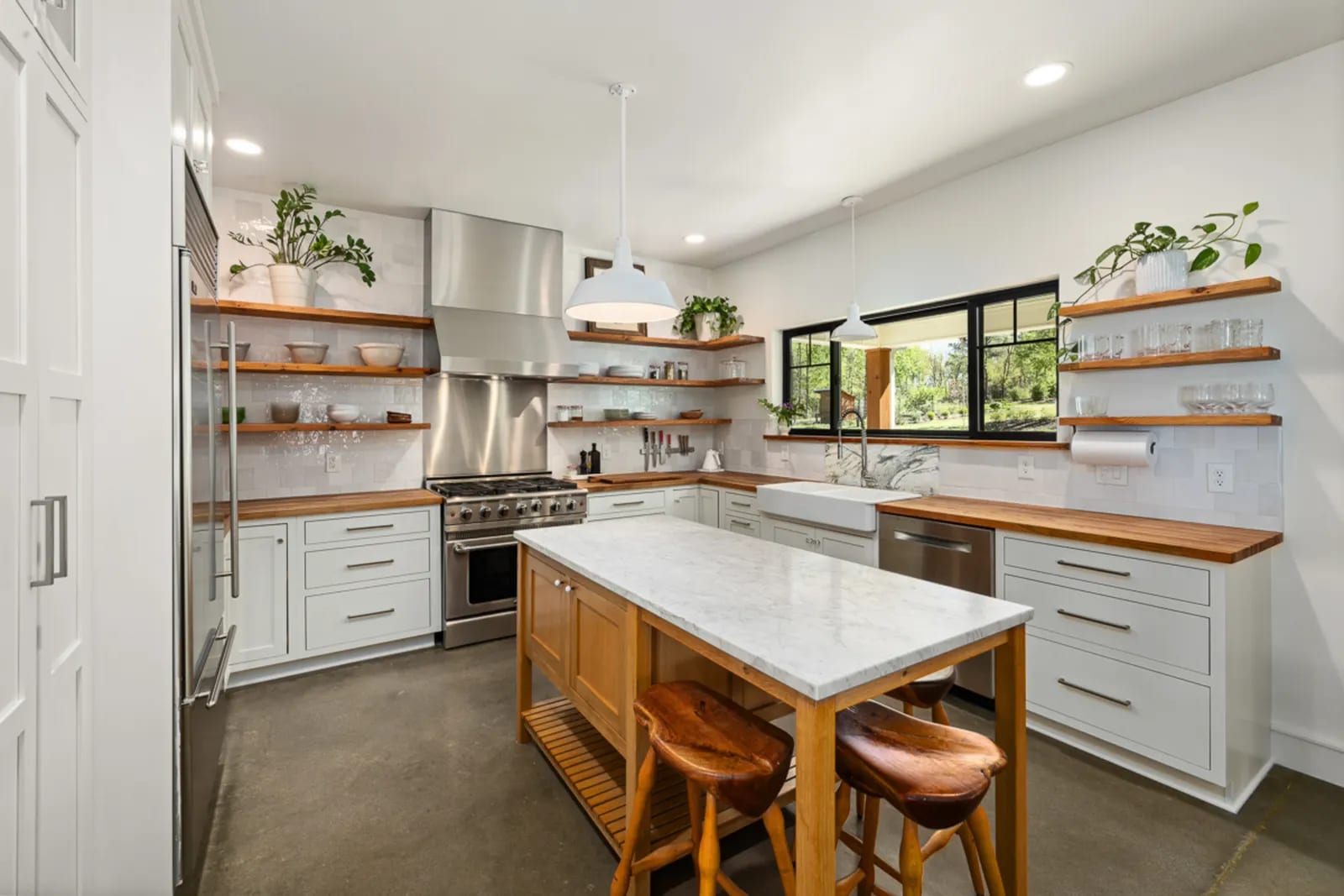 Cocina luminosa con isla de encimera de mármol blanco veteado, estanterías de madera y taburetes altos