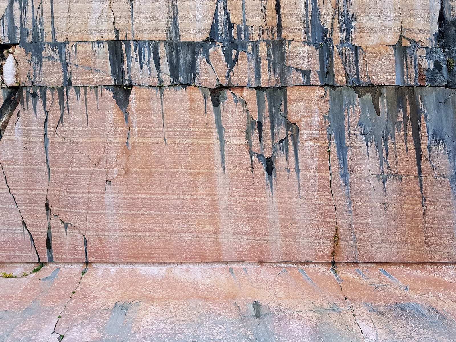 Frente cortado de una cantera de mármol rojizo, con bancos horizontales y regueros oscuros que bajan por la pared