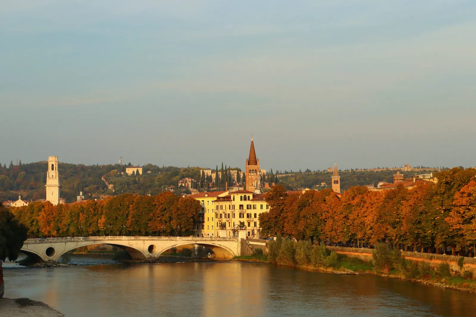 Puente sobre el río Adige en Verona, con una torre de iglesia y árboles de otoño en las orillas