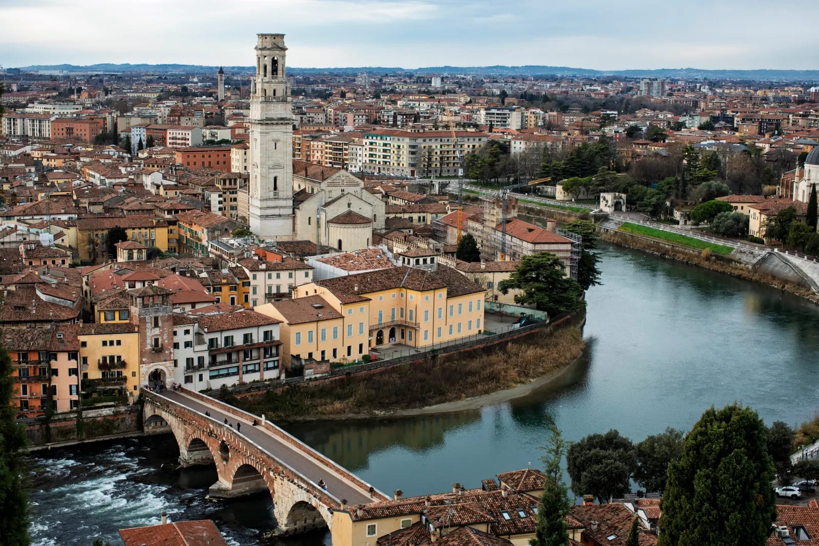 Vista aérea de Verona con el río Adige, un puente de piedra y la torre de la catedral entre tejados de tejas rojas