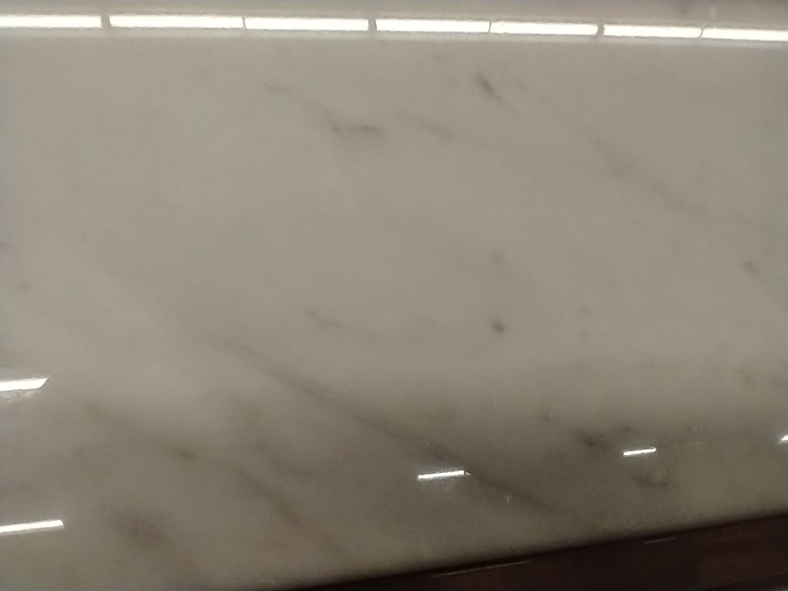 Primer plano de una losa de mármol blanco con vetas grises, pulida y con reflejos de luz