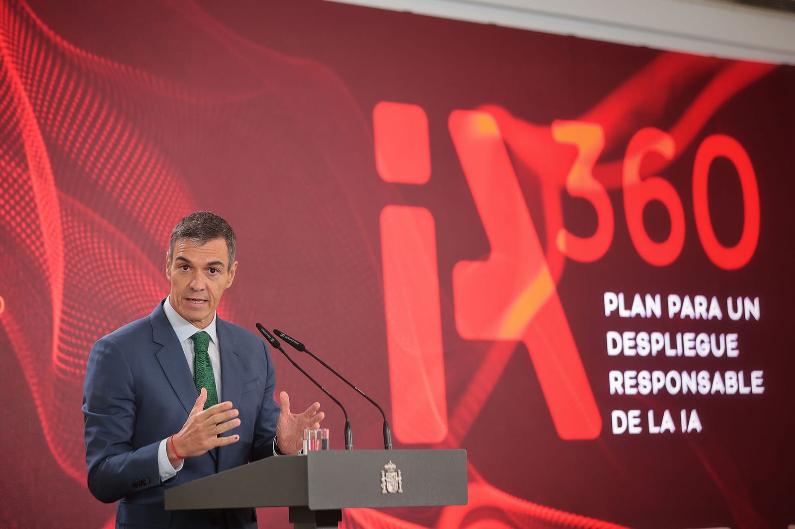 Pedro Sánchez gesticula tras un atril con el escudo de España, ante una pantalla roja con el rótulo iA360 y el título del plan