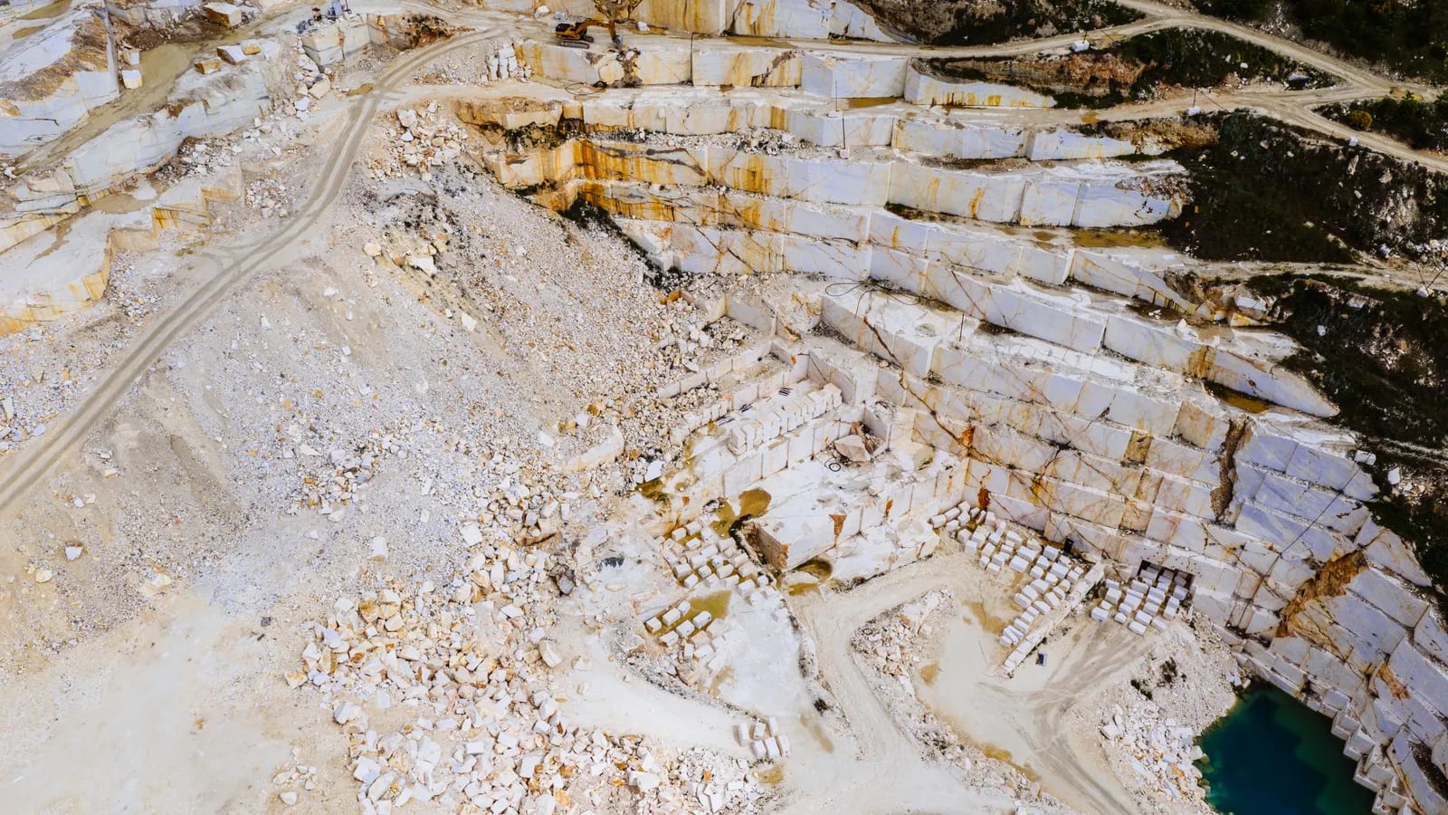 Vista aérea de una cantera de mármol con bancos escalonados de roca clara y bloques apilados en la explanada