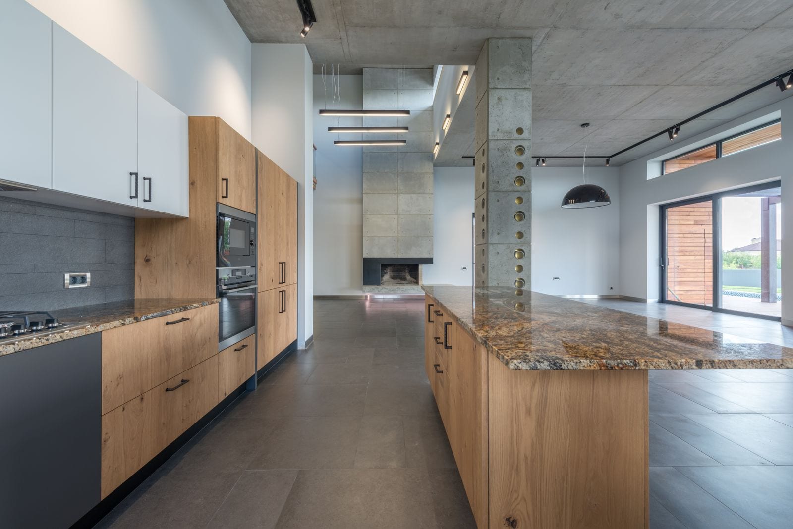 Cocina amplia de diseño con isla y encimera de piedra veteada en tonos dorados y marrones, muebles de madera y suelo gris