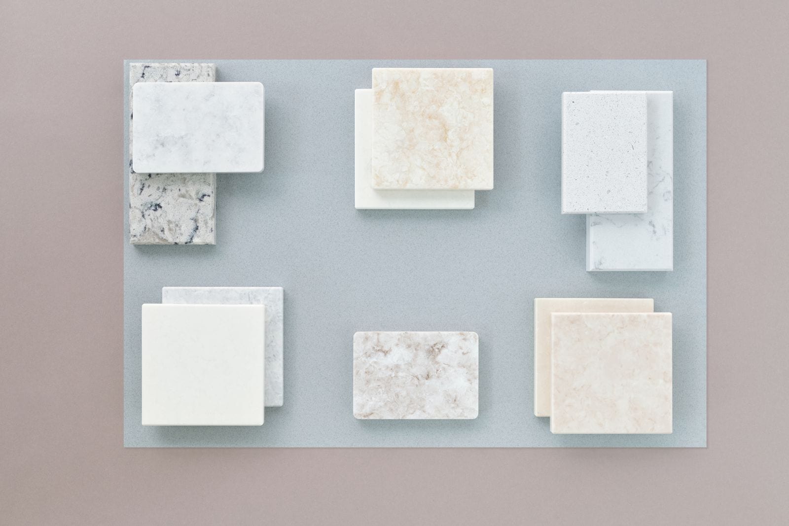 Muestras de placas de piedra y cuarzo en tonos blancos, beige y grises dispuestas sobre una superficie azul grisácea
