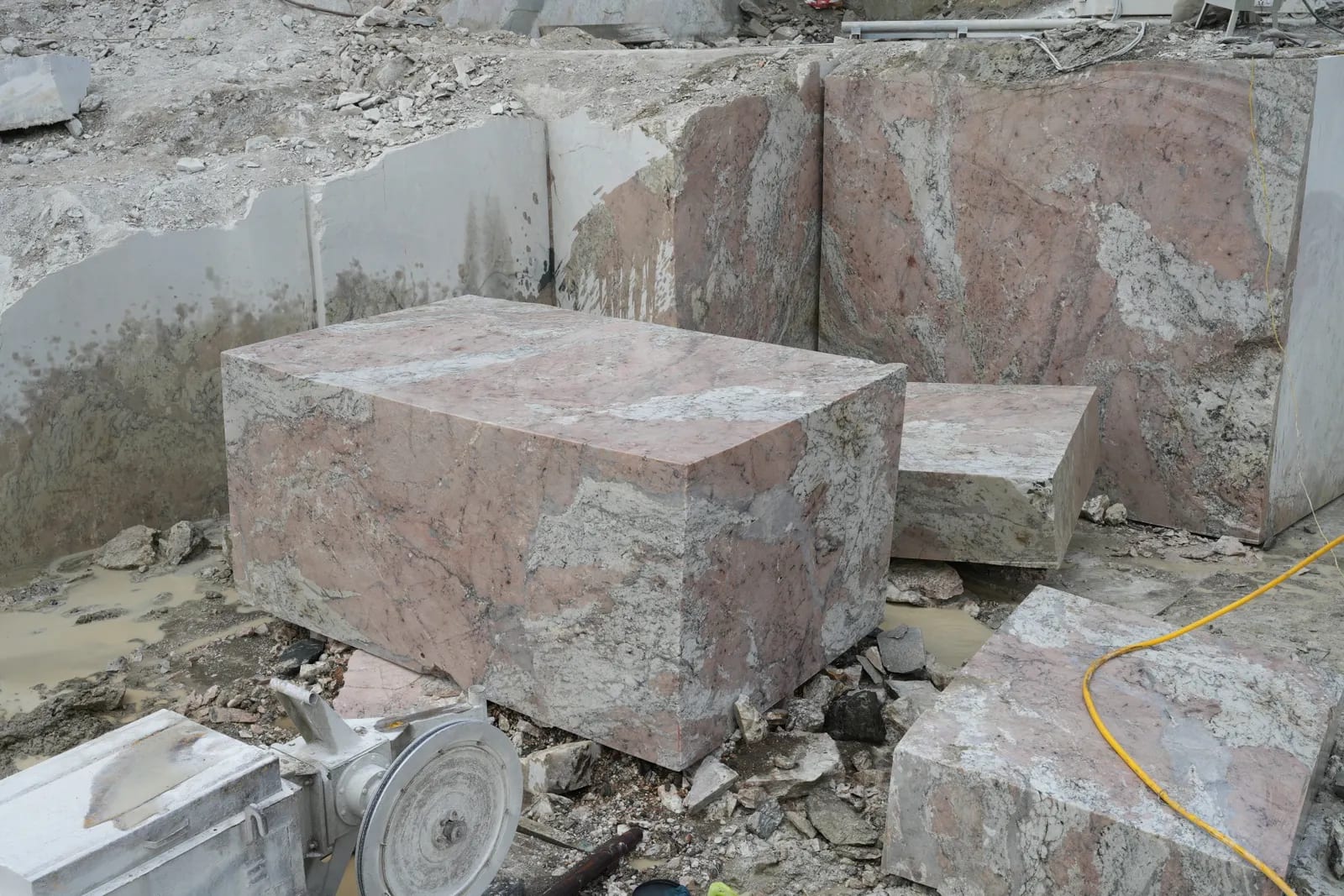 Grandes bloques de mármol rosado con vetas blancas en una cantera, con la polea de una máquina de hilo diamantado en primer término