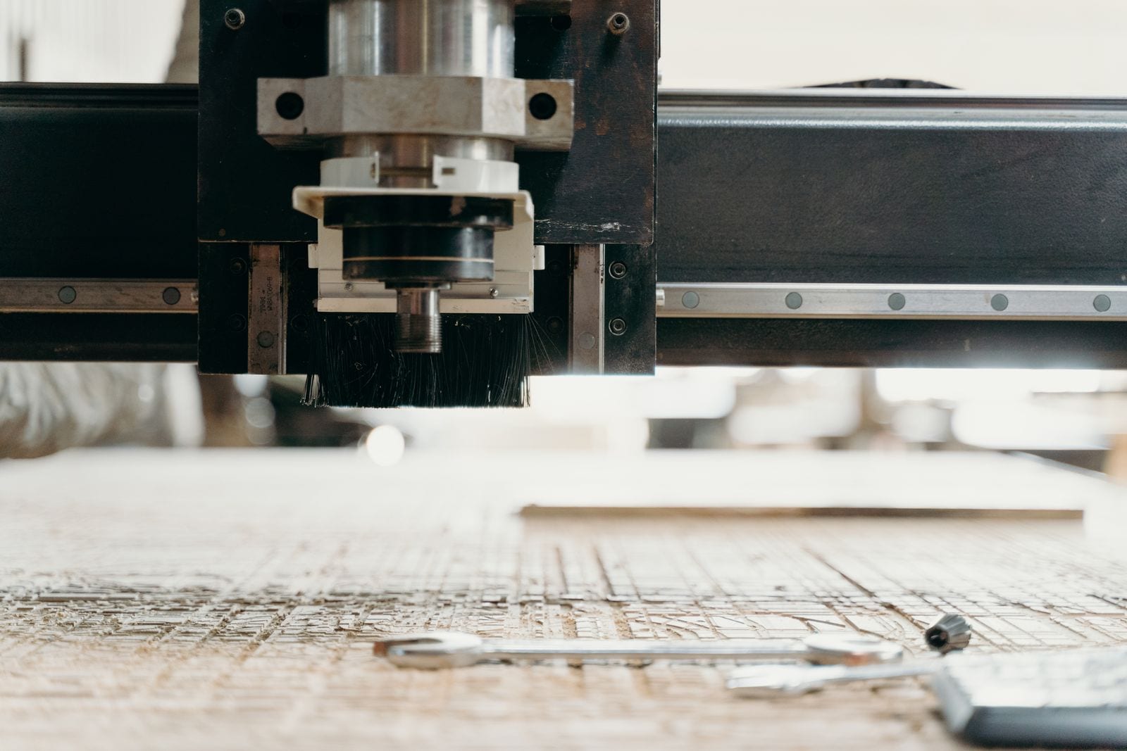 Cabezal de una fresadora CNC de pórtico con husillo y cepillo de aspiración sobre un tablero de madera mecanizado, con una llave fija sobre la mesa
