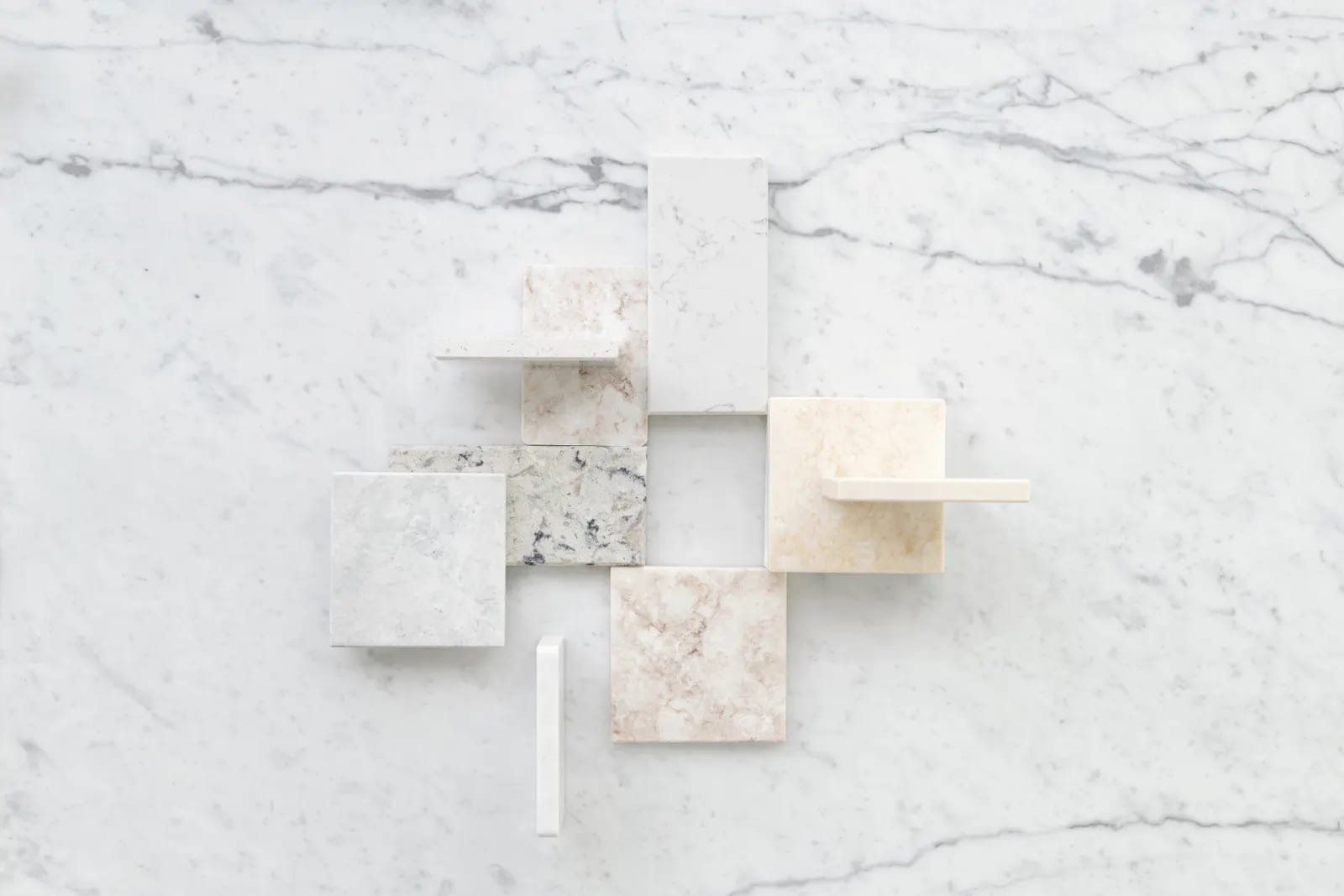 Vista cenital de muestras rectangulares de superficies en tonos blancos y beige sobre una plancha de mármol blanco con vetas grises