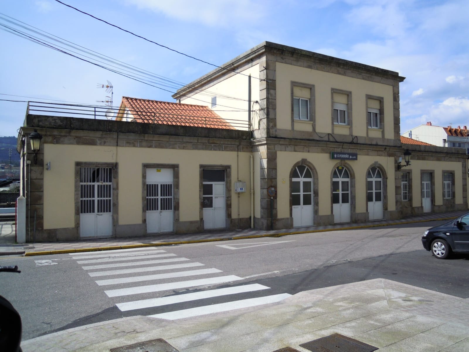 Fachada de la estación de ferrocarril de O Porriño, edificio de dos plantas con muros amarillos y recercos de piedra, junto a un paso de peatones