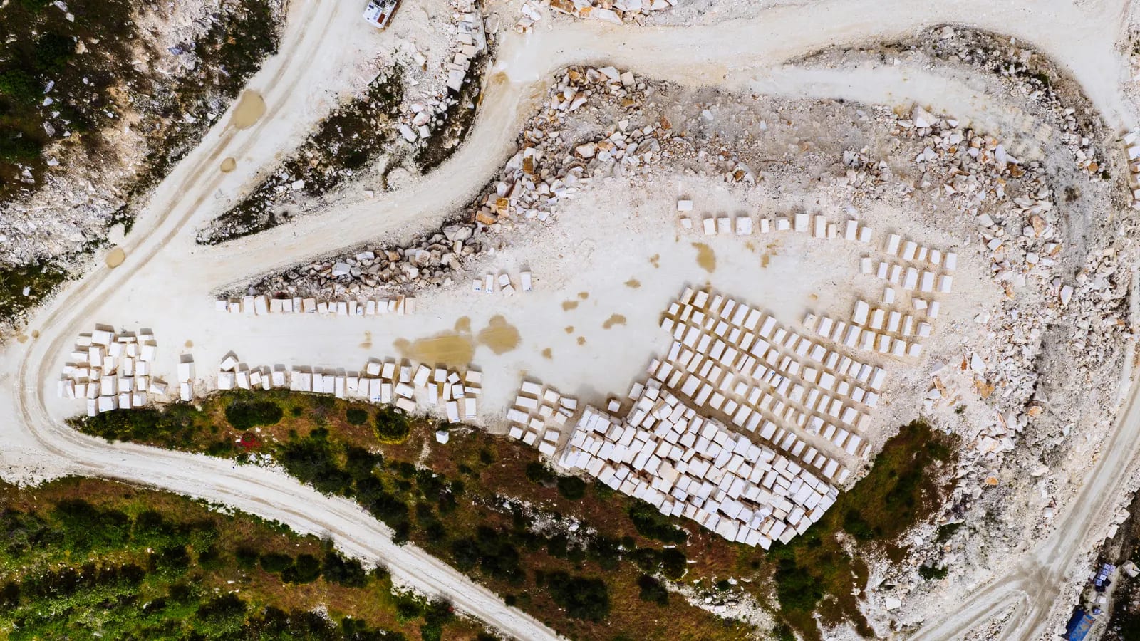 Vista aérea cenital de una cantera de mármol con filas ordenadas de bloques blancos sobre una explanada y pistas de tierra