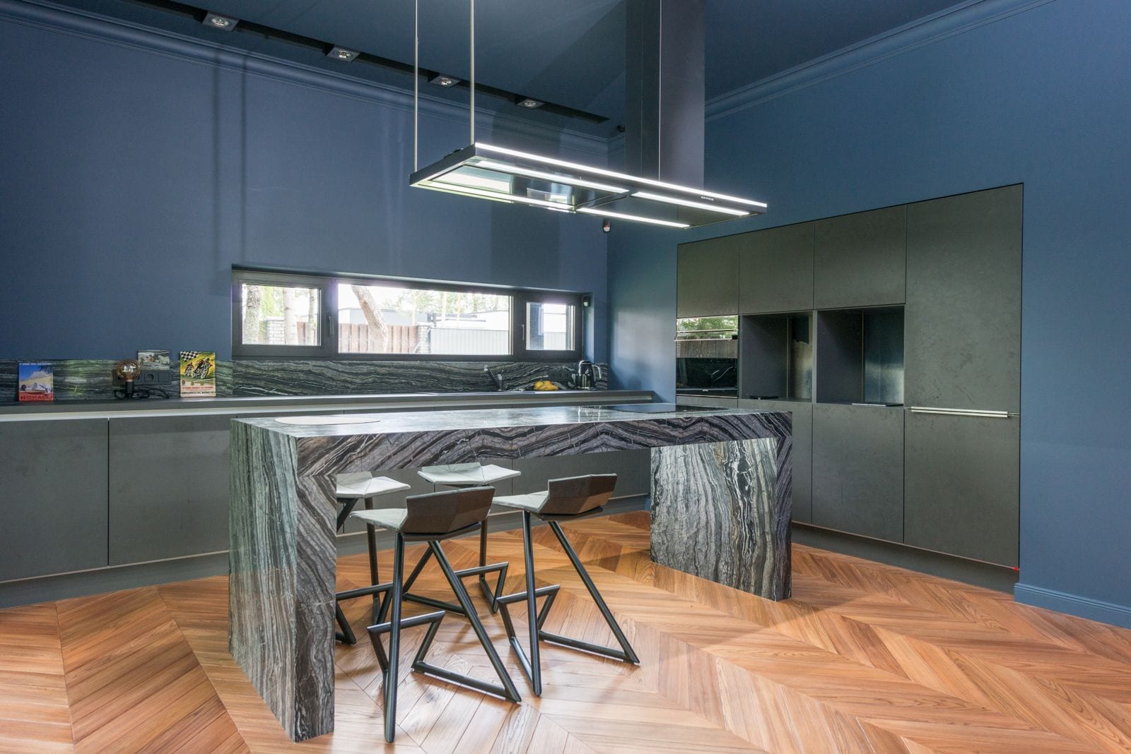 Cocina moderna de paredes azules con isla rematada en piedra veteada oscura y taburetes de diseño alrededor