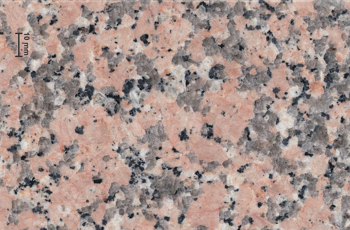 Superficie pulida de granito rosado de grano grueso con cristales grises y puntos negros y una regla de diez milímetros