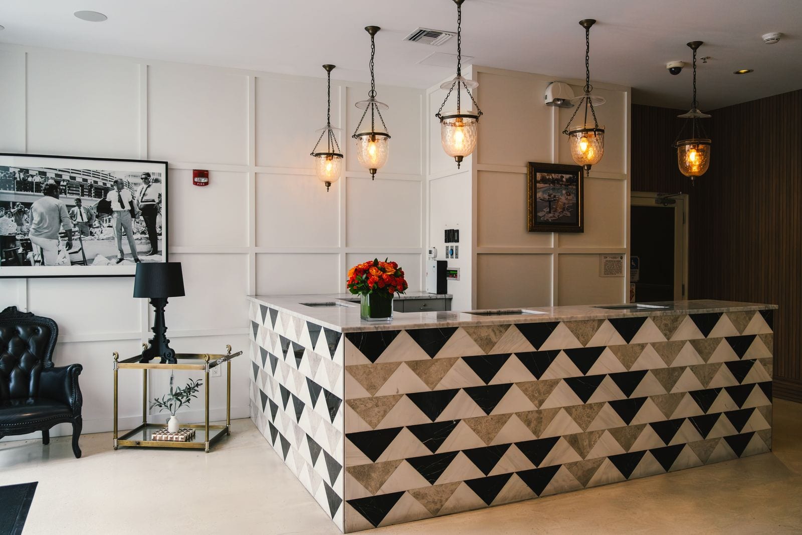 Mostrador de recepción de hotel revestido con triángulos de mármol blanco, negro y beige, bajo lámparas colgantes
