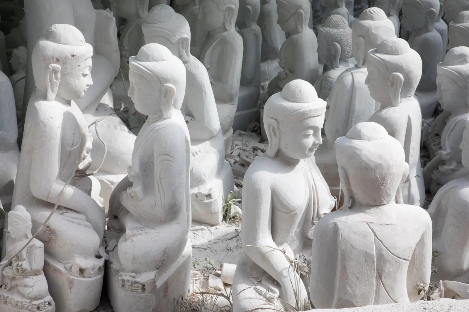 Hileras de estatuas de mármol blanco de figuras sentadas, a medio tallar, al aire libre bajo luz intensa