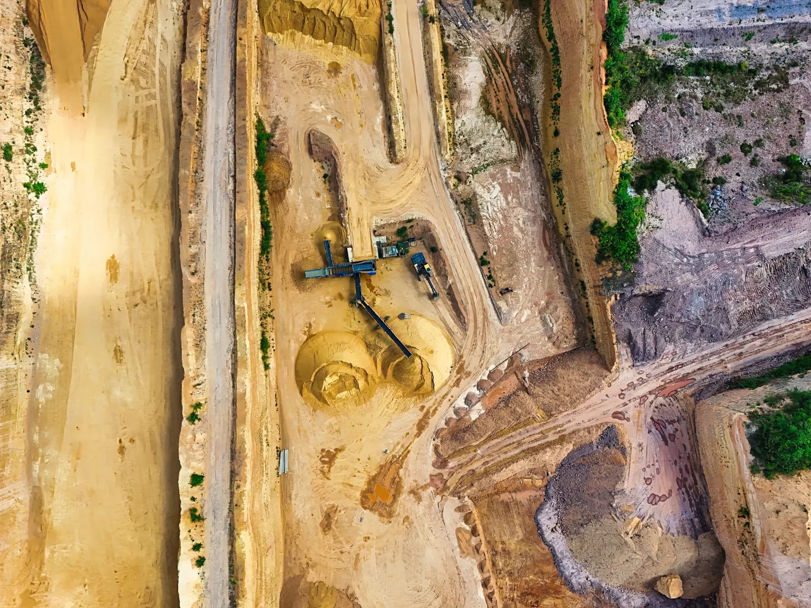 Vista aérea cenital de una explotación a cielo abierto con cintas transportadoras, montones de áridos, caminos y bancales de tierra ocre