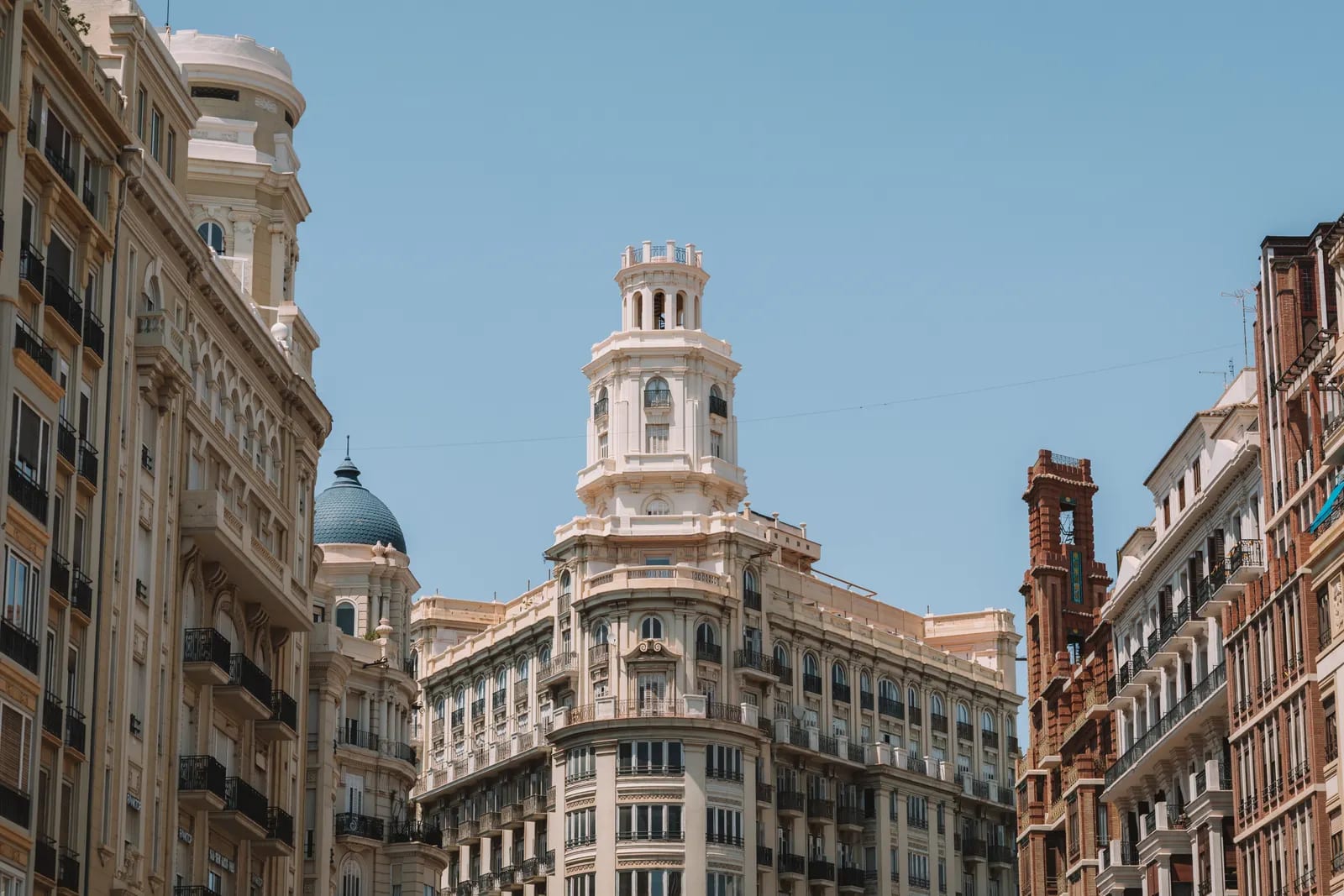 Edificios de fachada clara con torre y cúpula azul en una calle del centro de Valencia, bajo un cielo despejado